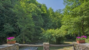 An outdoor seating area with stone walls and wooden chairs, surrounded by lush greenery and a small water feature. - Il Mulino di Cecco by Interhome (Vernio)