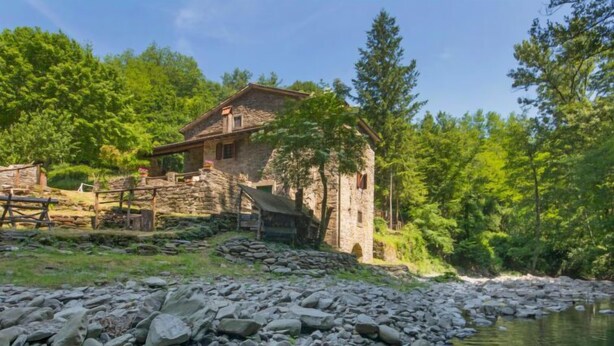 A rustic stone building with a stone staircase leading to a wooden door, surrounded by lush greenery and a rocky riverbank. - Il Mulino di Cecco by Interhome (Vernio)
