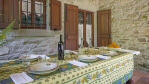 A rustic dining area with a stone wall, wooden shutters, and a table set with plates, glasses, and a bottle. - Il Mulino di Cecco by Interhome (Vernio)
