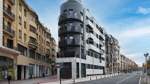 A modern building with a curved facade, multiple balconies, and a street view with pedestrians. - Gloria | The Rentals Collection (San Sebastián)