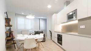 A modern kitchen with white cabinetry, a built-in microwave, and a dining area with a round table and chairs. - Gloria | The Rentals Collection (San Sebastián)