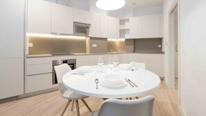 A modern kitchen with white cabinetry, a round dining table set for four, and a pendant light above. - Gloria | The Rentals Collection (San Sebastián)
