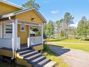 A wooden cabin with a porch, steps leading to the entrance, and a view of a forested area.