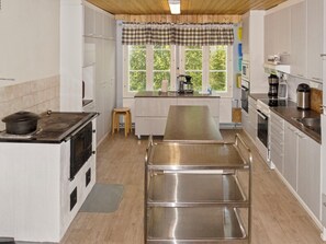 A kitchen with a large stainless steel counter, a stove, and a window with a view of greenery.