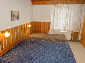 Et værelse med træpaneler, to senge med mønstret sengetøj, en radiator og et vindue med blomstrede gardiner.