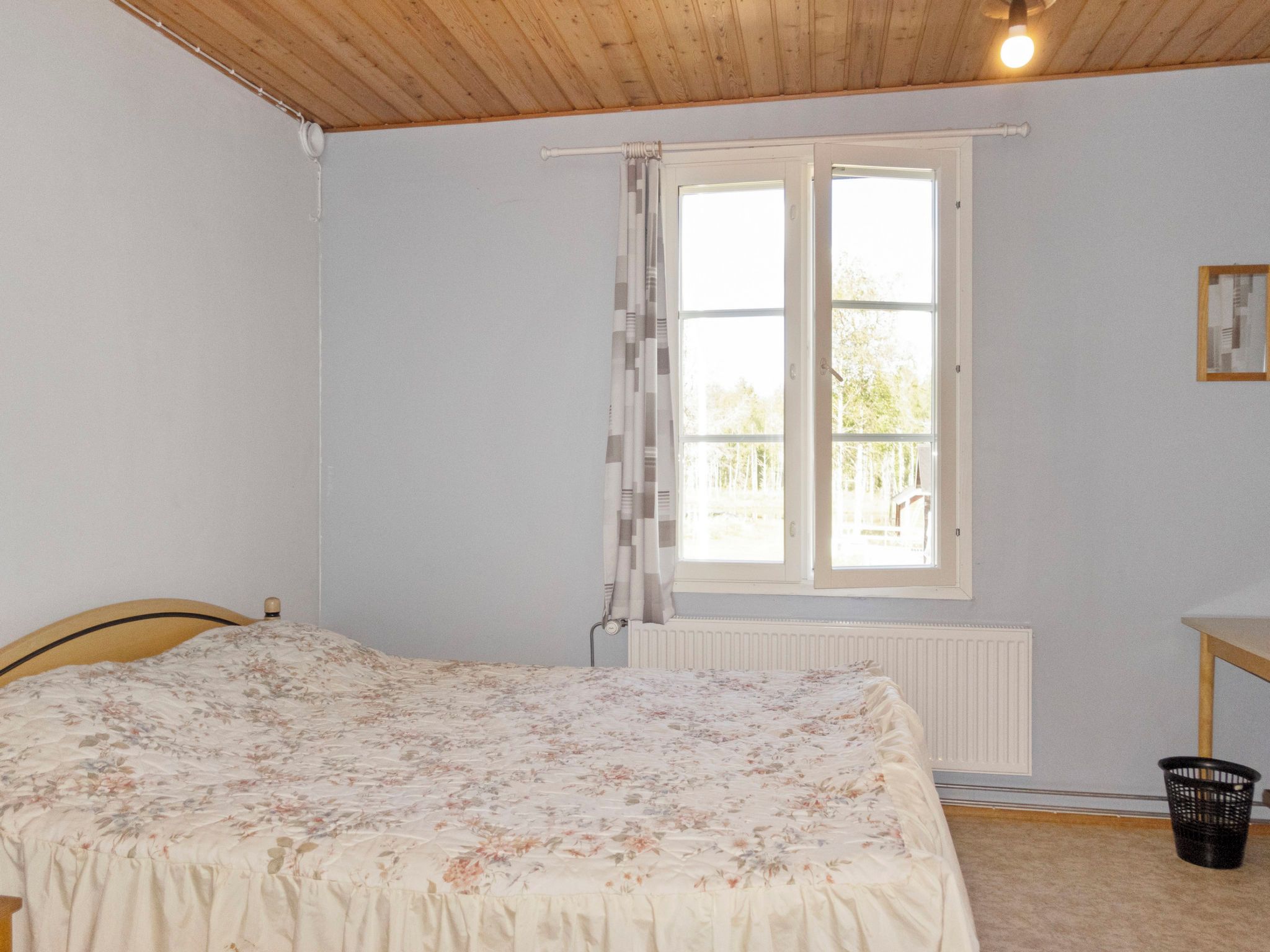 Una camera da letto con un letto, una finestra con tende, un termosifone e un tavolino.