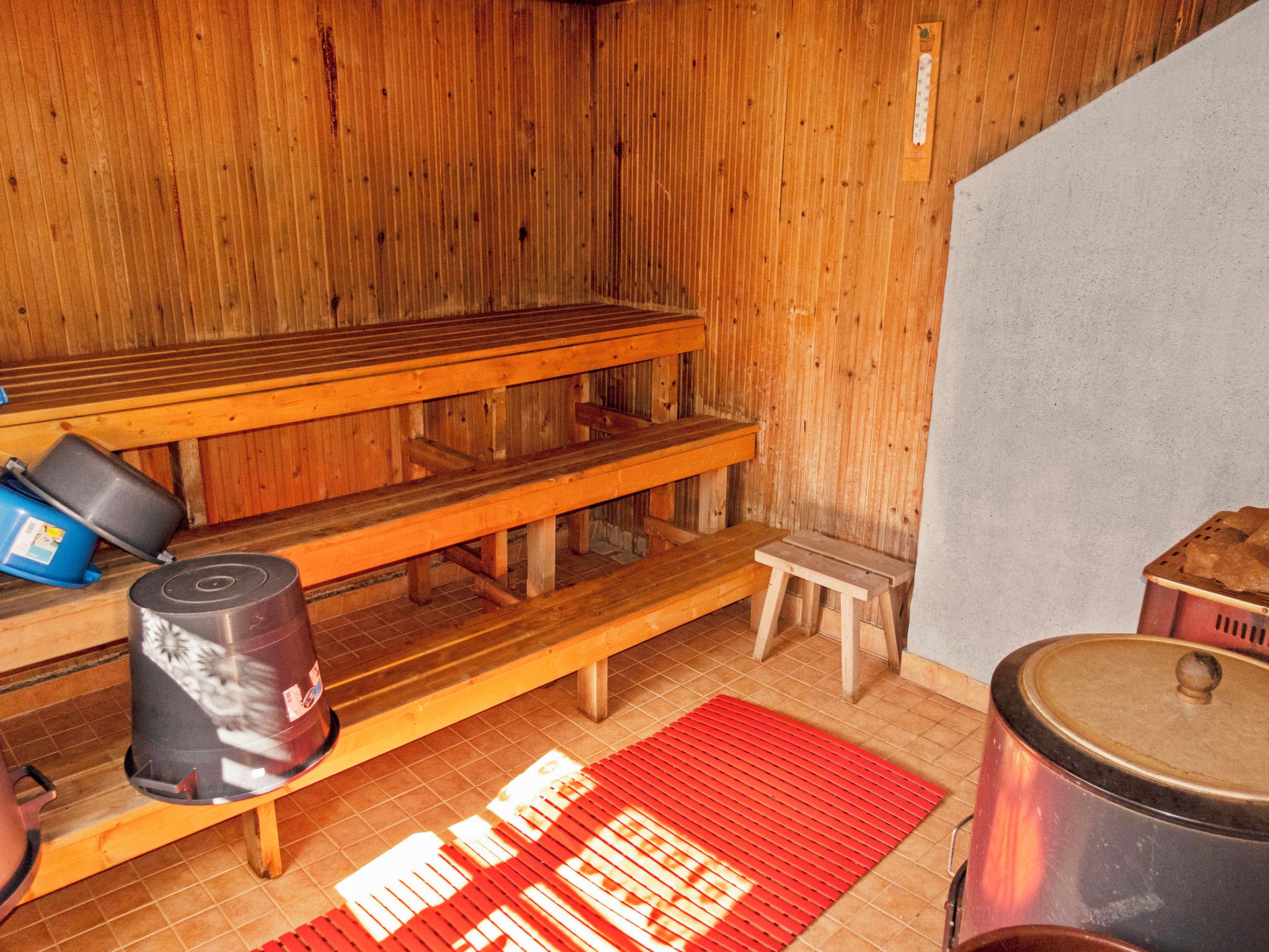 Et sauna-rum med træbænke, en rød måtte og en stor metalbeholder.