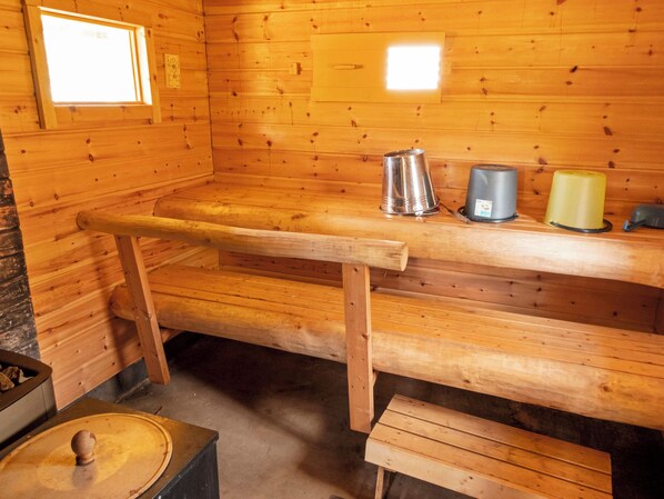 A wooden cabin interior with a bench, a metal kettle, and a yellow container on a shelf.