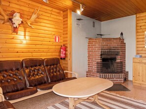 A log cabin interior with a leather sofa, a round table, a brick fireplace, and a fire extinguisher mounted on the wall.