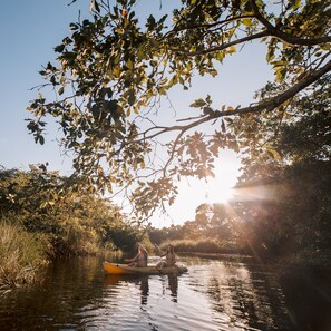 A river scene with two people in a canoe, surrounded by trees and sunlight.