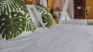 Una cama con ropa de cama blanca y almohadas con estampado de hojas verdes.