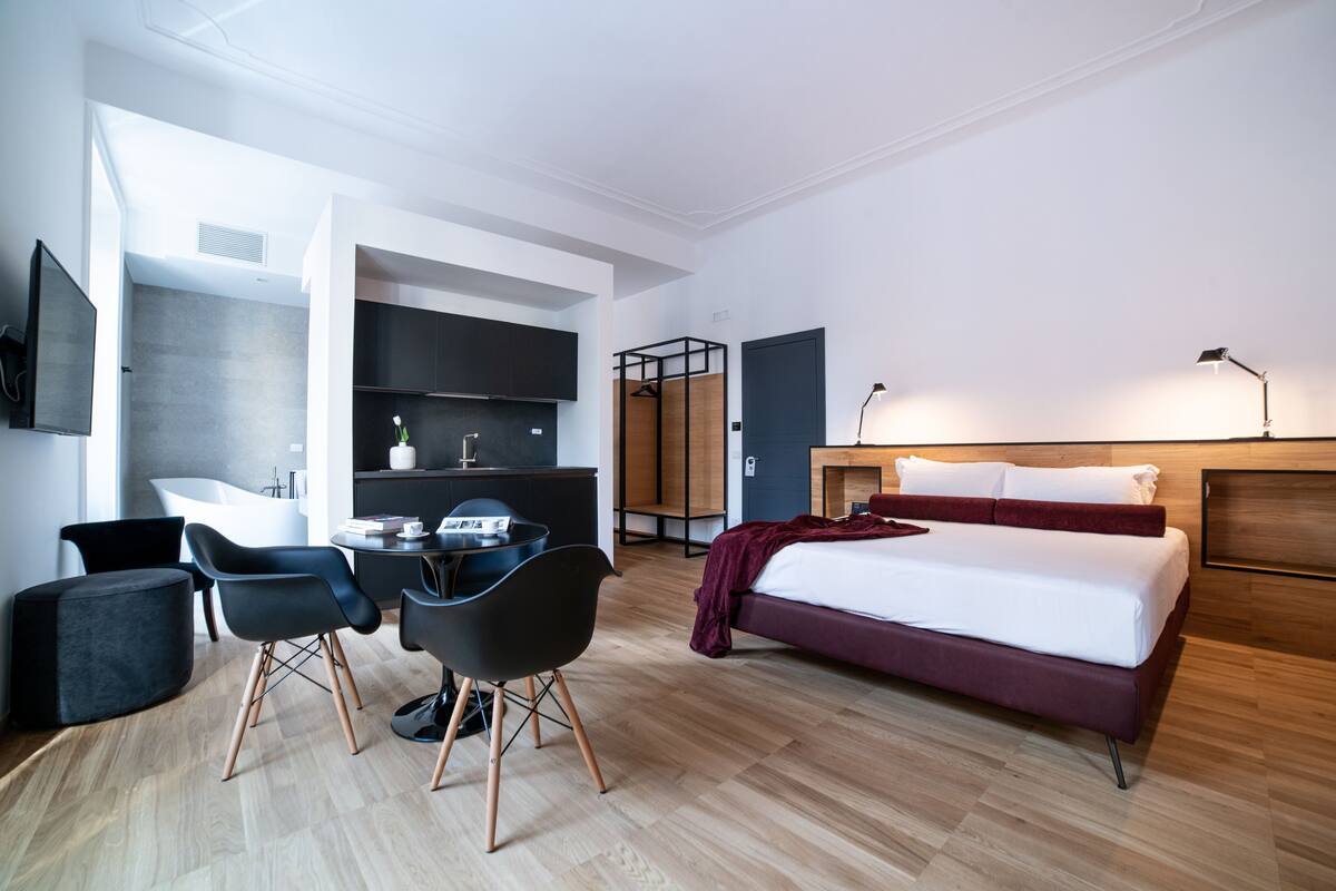 A modern hotel room with a bed, desk, chairs, and a TV.