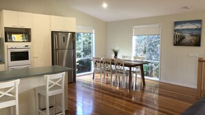 Una cocina moderna con armarios blancos, un refrigerador de acero inoxidable y un horno. Hay un comedor con una mesa de madera y sillas blancas.