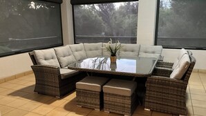 Un sofá sectional en esquina con una mesita de centro de vidrio, reposapiés acolchados y una planta en maceta.