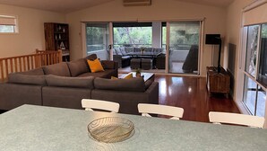 Una sala de estar moderna con un sofá seccional, una mesa de comedor con sillas y un amplio ventanal corredizo que da a un patio exterior.