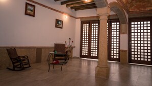 Une pièce spacieuse avec un plafond haut, des poutres en bois, une colonne en pierre et une porte en bois traditionnelle ornée d’un motif en treillis.