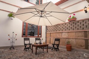 Un patio al aire libre con una mesa y sillas, un paraguas grande y plantas en macetas.