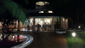 Een nachtzicht van een hotel met een rond gebouw, een zwembad en palmbomen.
