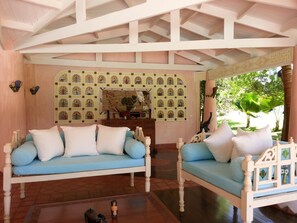 Une pièce avec un plafond en bois, un canapé bleu avec des coussins blancs, une petite table ornée d’objets décoratifs et un mur à motifs.