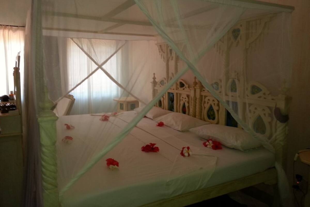 Un lit à baldaquin, avec une literie blanche et des fleurs rouges.