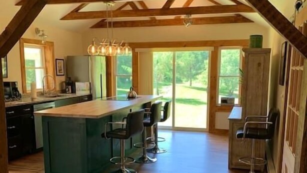 A spacious kitchen with a central island, bar stools, and large windows offering a view of the outdoors.