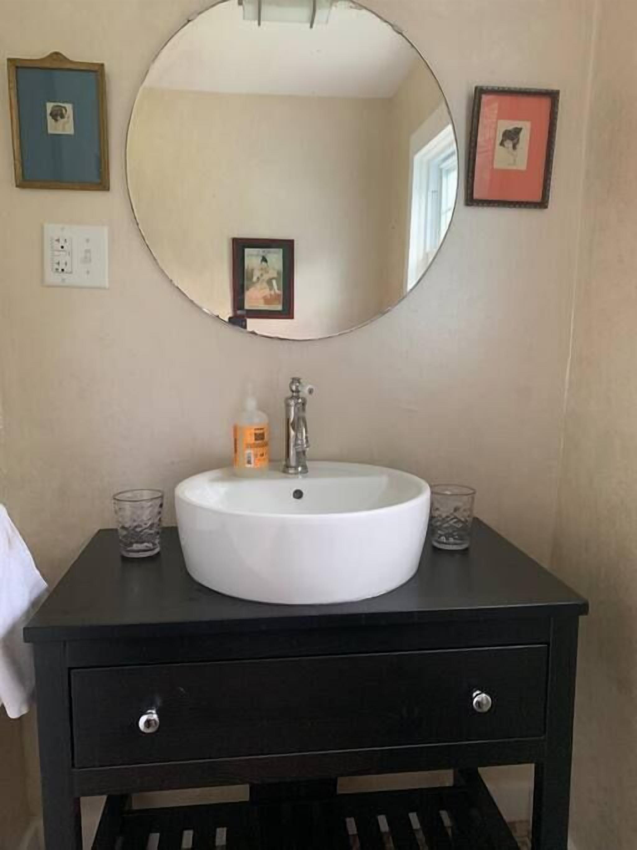 A bathroom vanity with a white sink, a mirror, and two framed pictures on the wall.