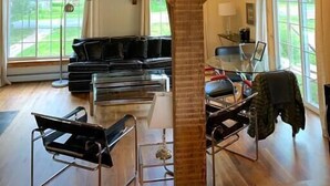 A spacious room with a high ceiling, wooden beams, a black leather sofa, a glass coffee table, and a modern chair.