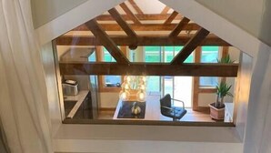 A room with a sloped ceiling, a window with a view of the outside, and a wooden floor.