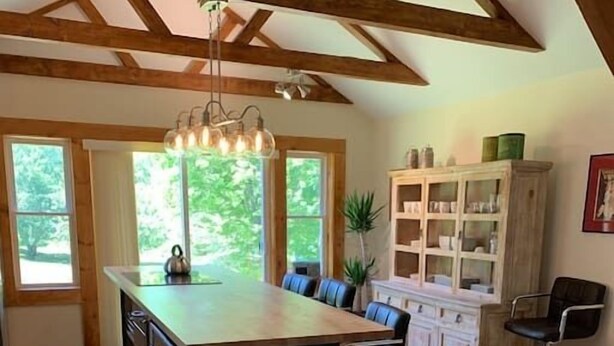 Une cuisine spacieuse dotée d’un grand îlot central, de poutres en bois au plafond et offrant une vue sur la verdure environnante.