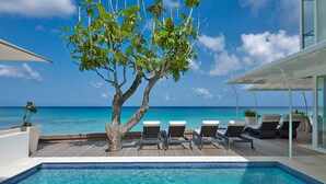Un espace aménagé au bord de la piscine, avec vue sur l’océan, des chaises longues et un arbre.