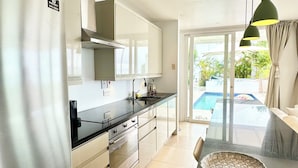 Une cuisine moderne dotée d’appareils électroménagers en acier inoxydable, d’un îlot central en verre et offrant une vue sur une piscine.
