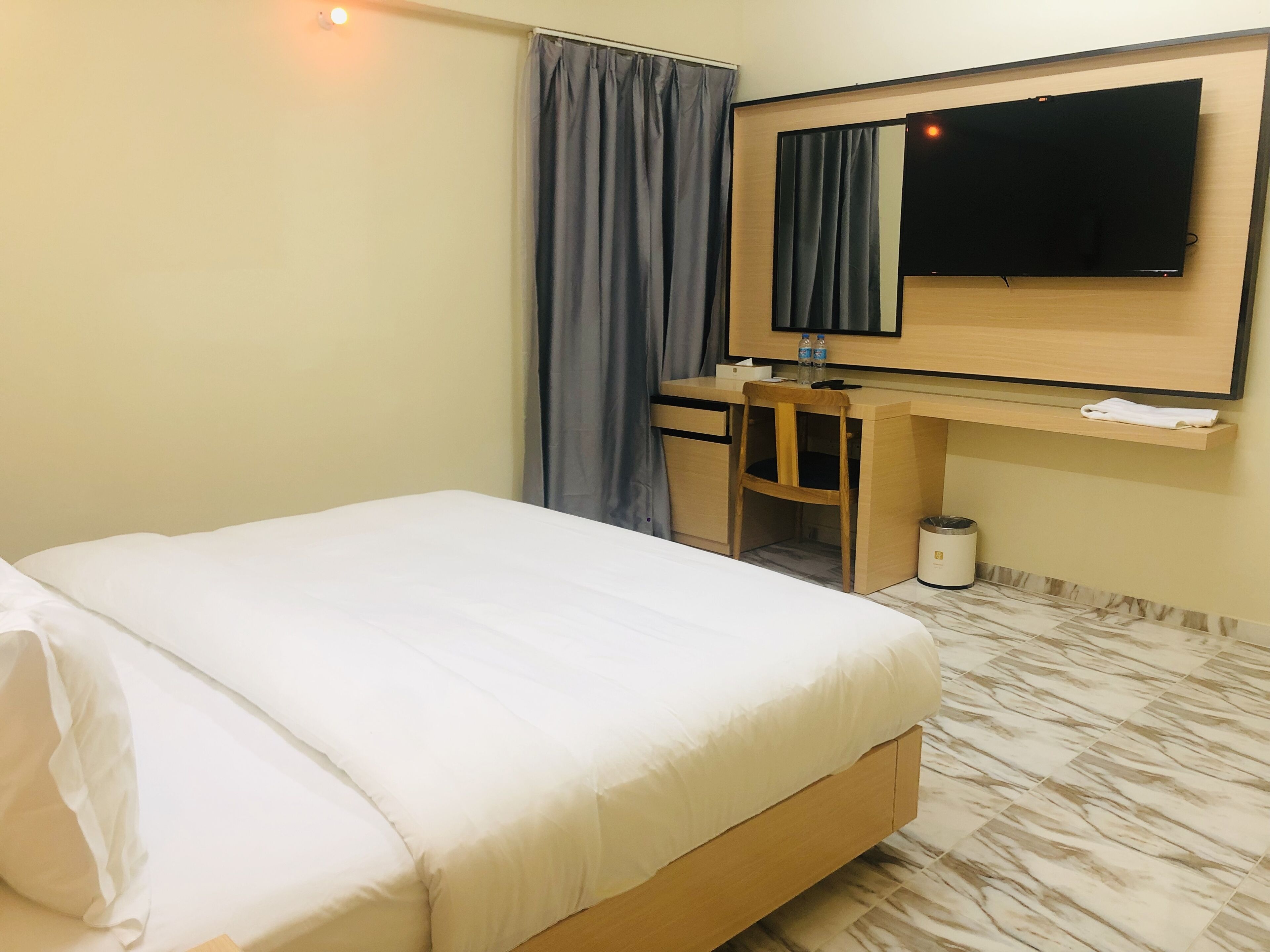 A hotel room with a bed, a desk, a chair, a television, and a trash bin.
