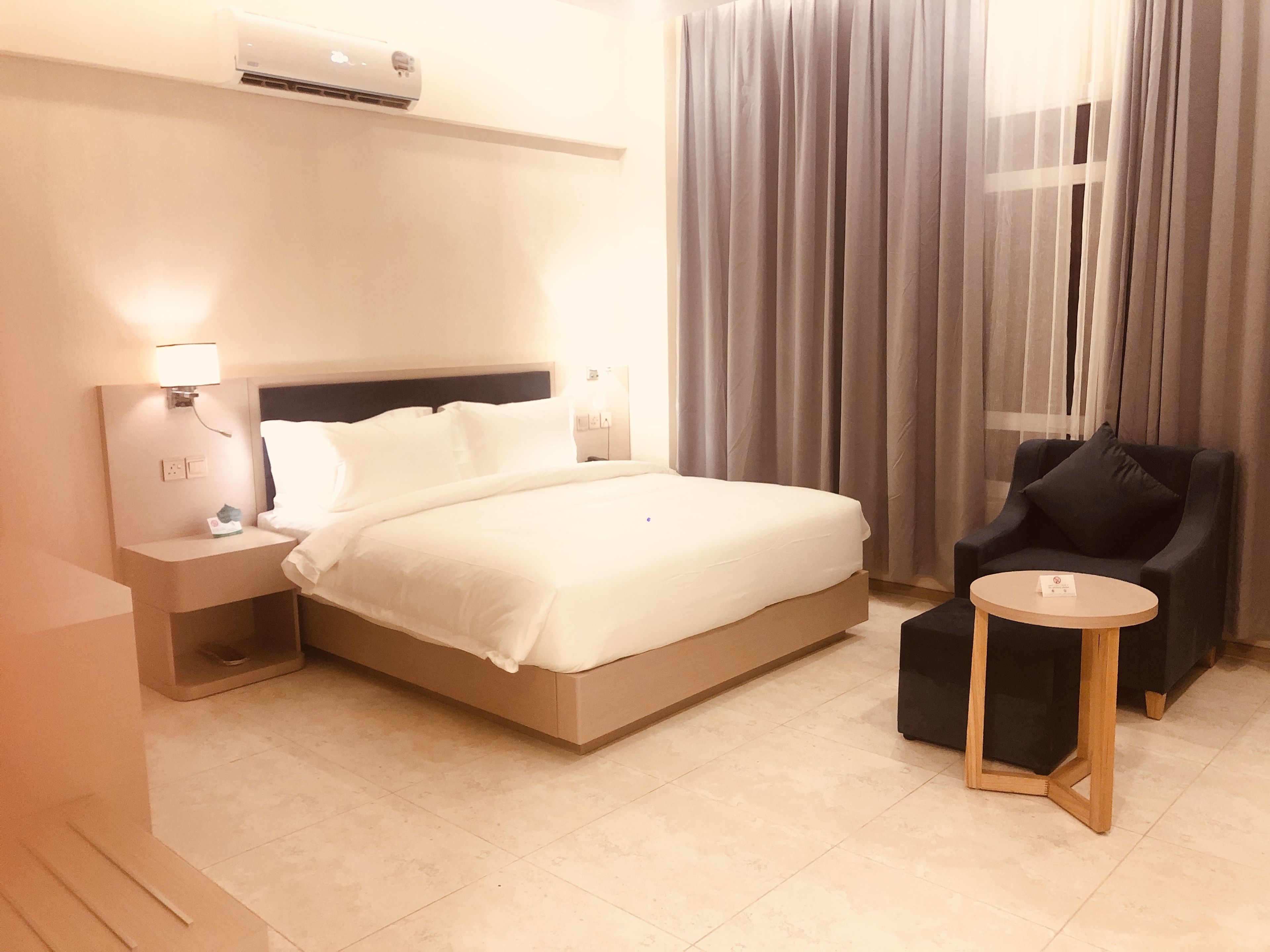 Una habitación de hotel con una cama, una mesita de noche con lámpara, una silla y una pequeña mesa.