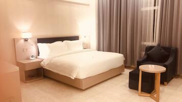Una habitación de hotel con una cama, una mesita de noche con lámpara, una silla y una pequeña mesa.