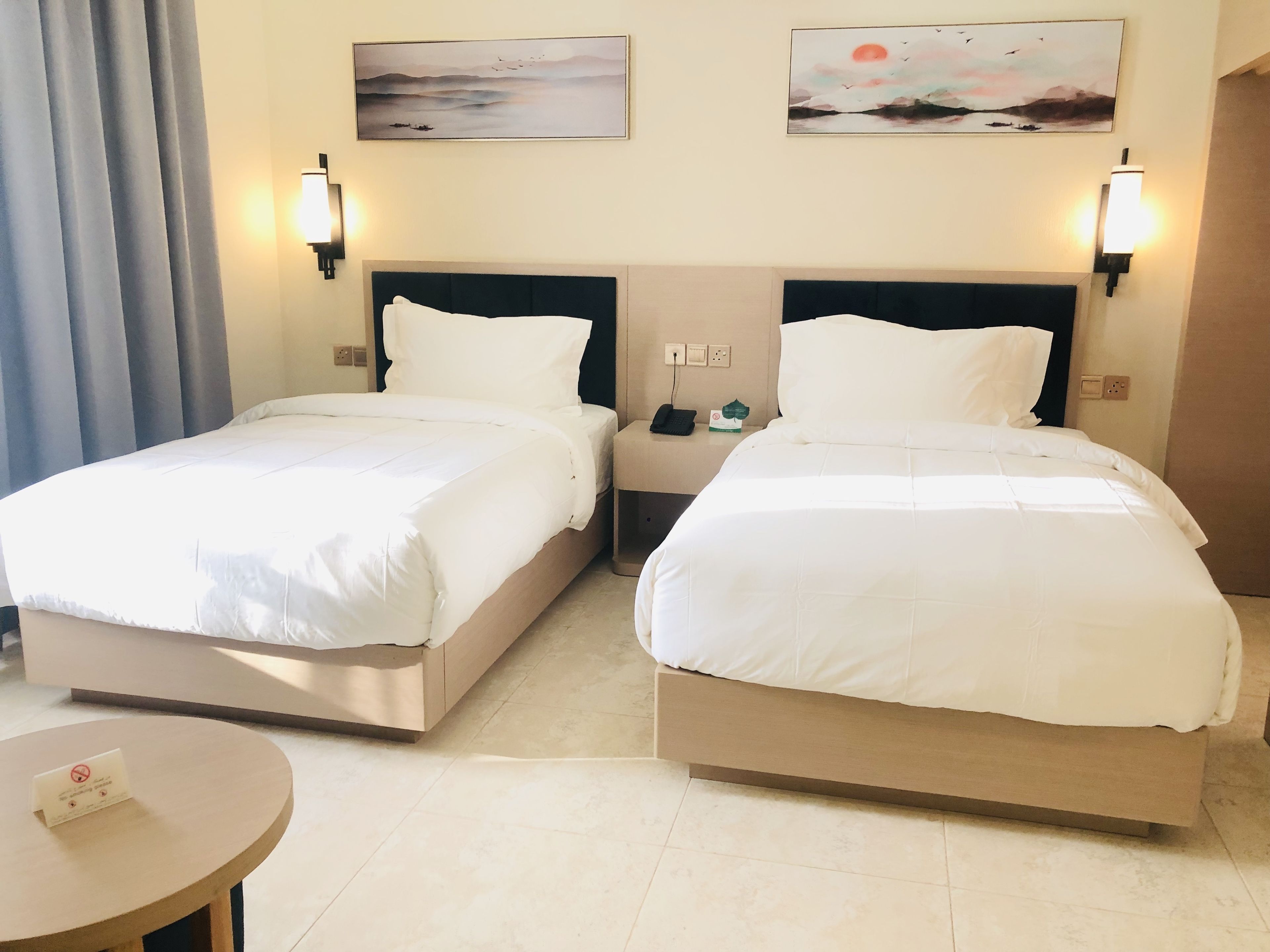 Habitación de hotel con dos camas, una mesita y obras de arte en las paredes.