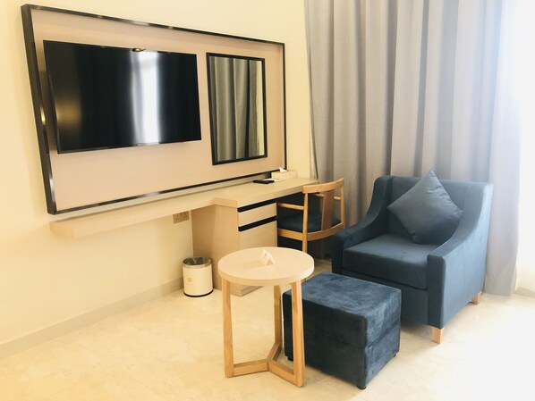 A modern living room with a flat-screen TV, a blue sofa, a small round table, and a wooden ottoman.