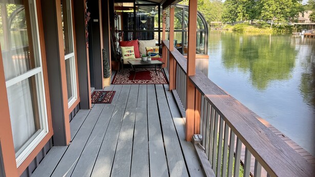Eine Holzterrasse mit einer Couch und einem kleinen Tisch, mit Blick auf einen ruhigen See.