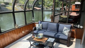 Ein gemütlicher Sitzbereich im Freien mit einem Korbsessel, einem Glastisch und Blick auf einen See durch große Fenster.