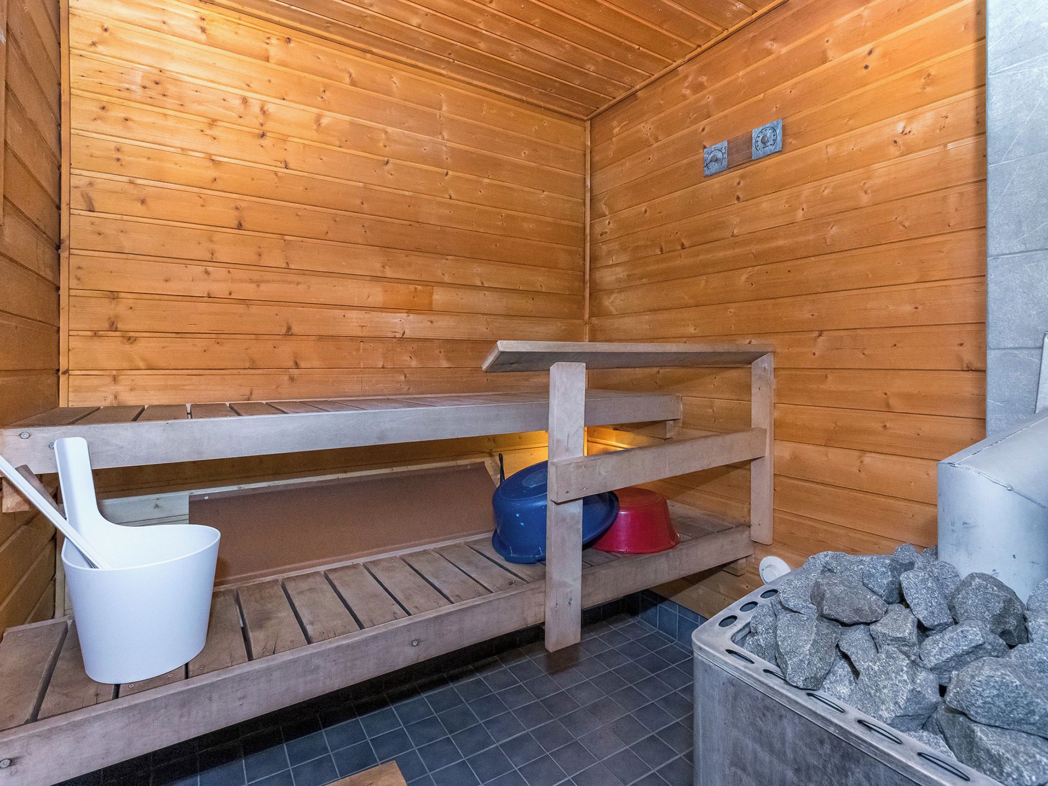 A sauna room with wooden walls, a bench, a white basin, and a stone container.