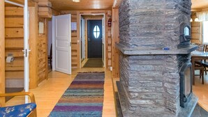 A wooden cabin interior with a stone fireplace, wooden floors, and a door leading to another room. - Vesan villa by Interhome (Sysmä)