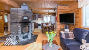 A cozy cabin interior with a stone fireplace, wooden walls, a dining area, and a living room with a sofa and a TV. - Vesan villa by Interhome (Sysmä)