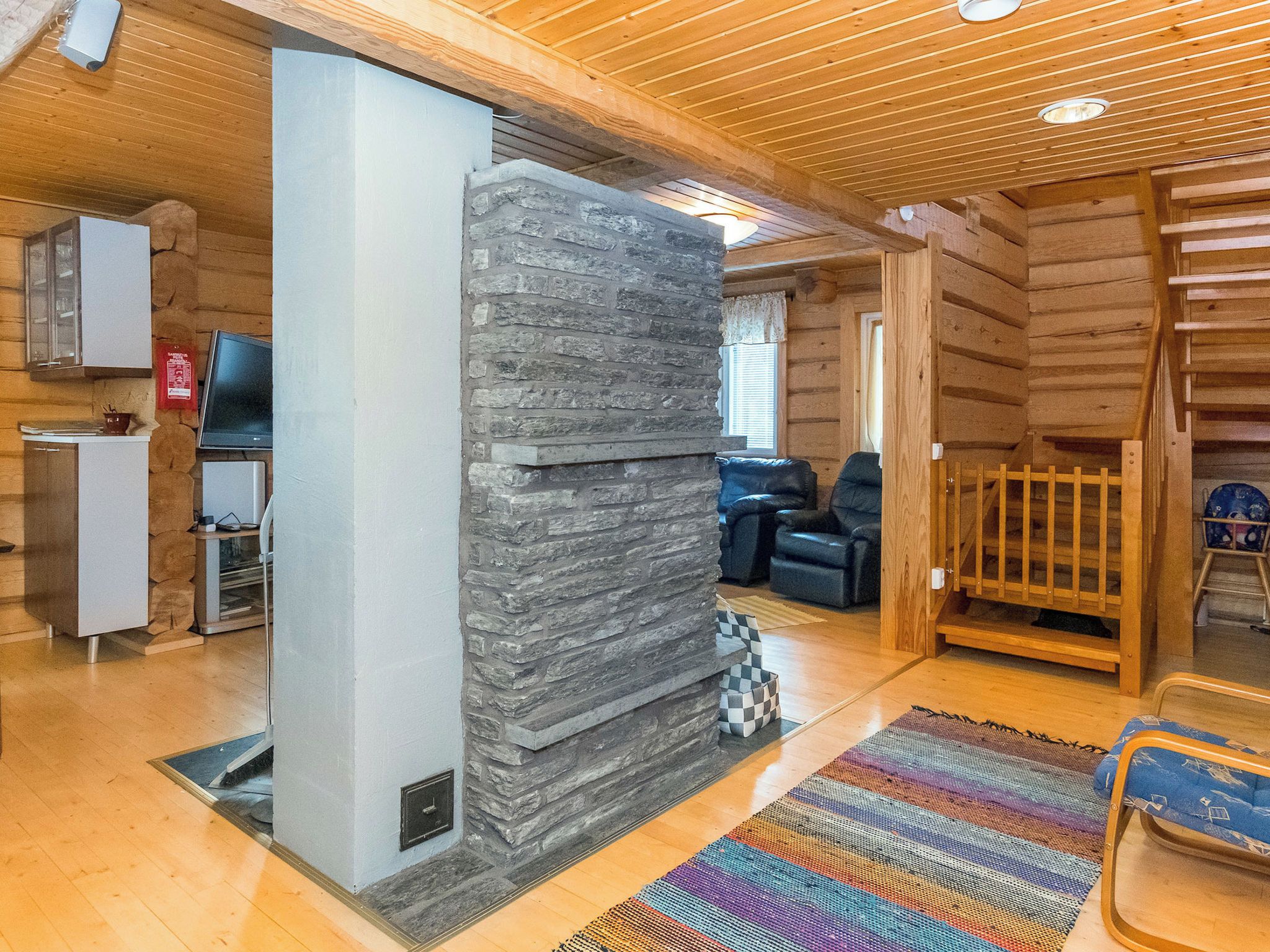 Een vakantiehuisje van hout met een stenen open haard, een eethoek en een woonkamer met een bank en stoelen.