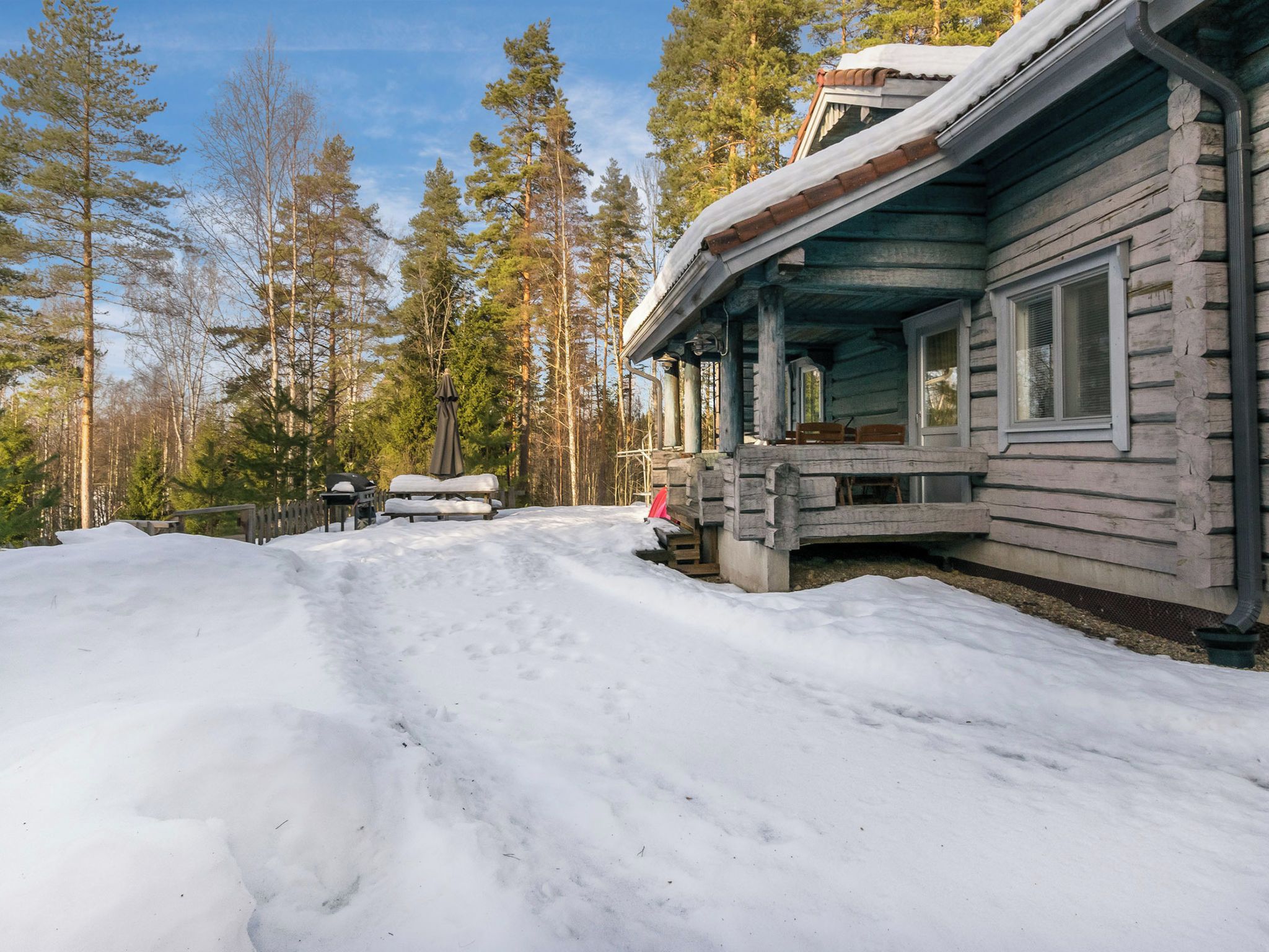 A log cabin with a porch, surrounded by snow and trees.