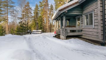 A log cabin with a porch, surrounded by snow and trees.