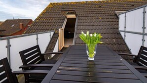 Una terraza en la azotea con mesa y sillas, un florero de vidrio con flores y vistas a edificios cercanos.