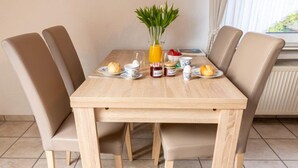 Una mesa de comedor con cuatro sillas, un florero con plantas verdes y alimentos para el desayuno, como tostadas, huevos y jugo.