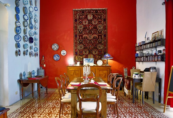 Un comedor con una pared roja, un tapete estampado y varios platos azules y blancos en la pared.