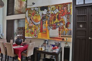 Un comedor con una mesa dispuesta para dos personas, una cafetera y un cuadro decorativo en la pared.
