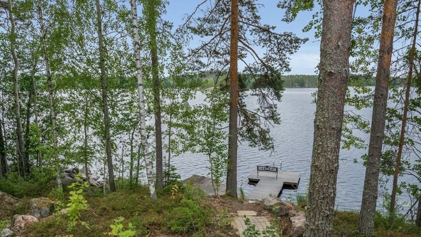 Eine Holzhütte am Seeufer mit einem Steg, der ins Wasser führt, umgeben von dichtem Wald.
