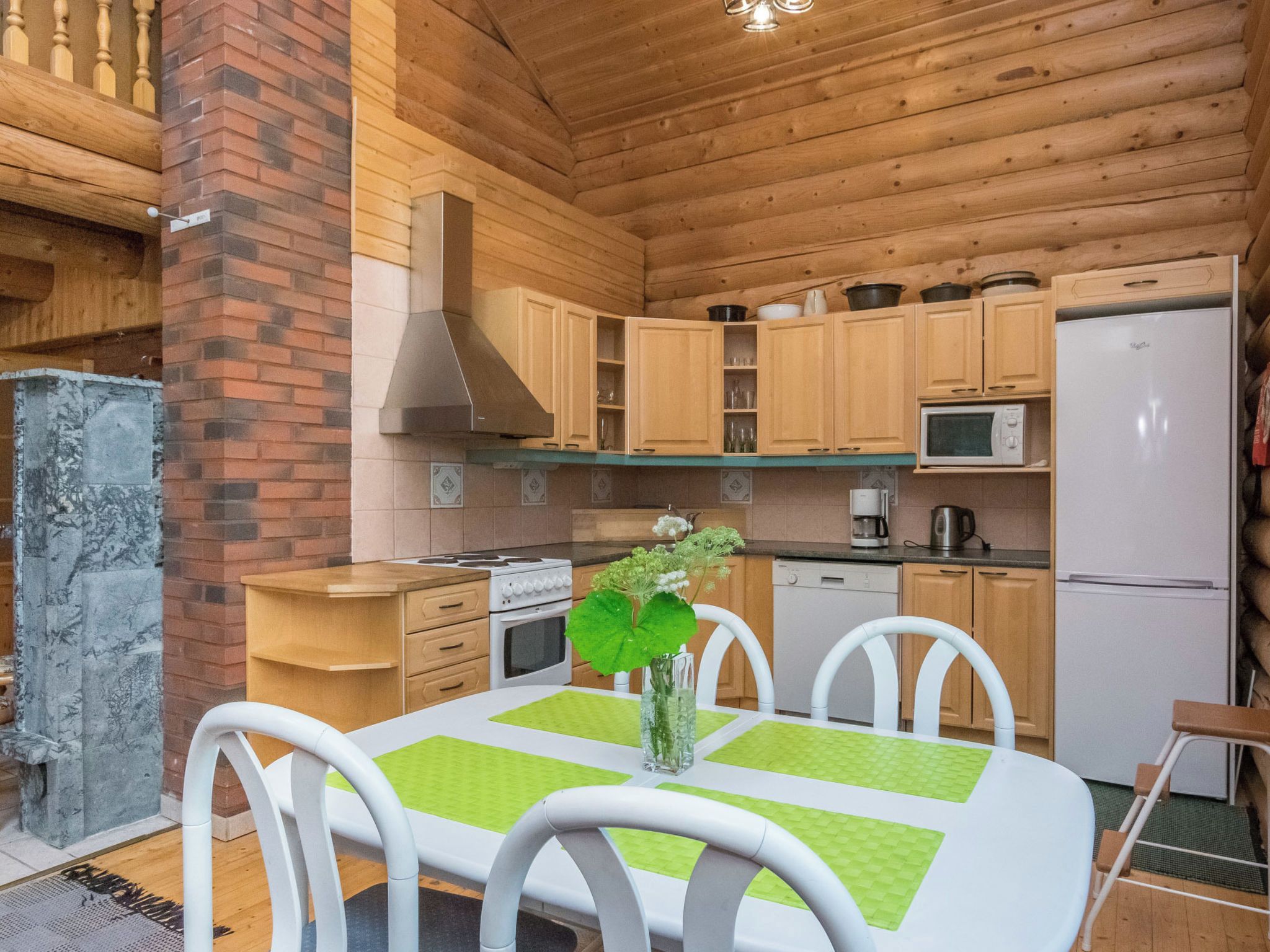 A wooden cabin interior with a kitchen, dining table, chairs, and a fireplace.